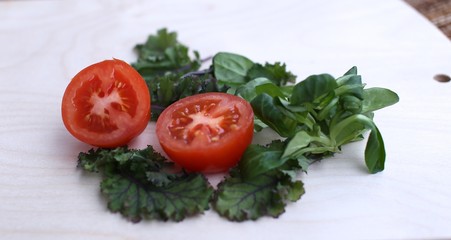 Tomato cut into two parts and spinach green fresh on wood board view from above