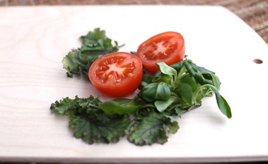 Spinach fresh, other greens and tomato cut into two pieces on wooden board