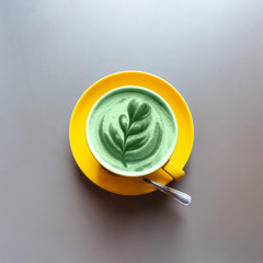 Flat lay of yellow hot trendy green latte with art flower petals on the foam on grey wooden table background