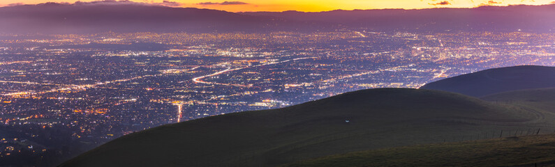 Panoramic night view of San Jose, Silicon Valley; the downtown area buildings visible on the right; green hills partially blocking the view; San Francisco Bay Area, California - obrazy, fototapety, plakaty