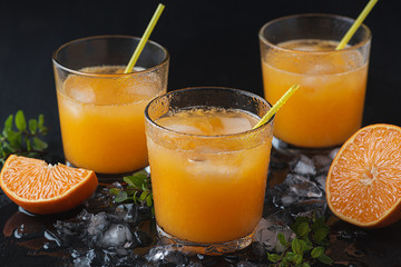  Tangerine cocktails with sliced mandarins, ice, mint on a black wooden table