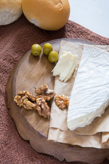 vertical photo, brie cheese with nuts and olives lies on a wooden board near freshly rolled buns