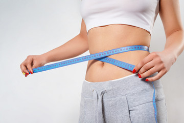 a young slender woman measures her waist with a centimeter tape. on white background