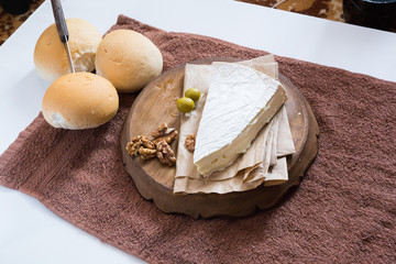 horizontal photo, brie cheese with nuts and olives lies on a wooden board near freshly rolled buns and a knife