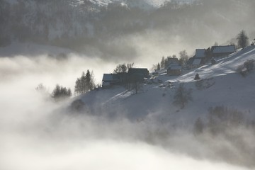 Snowy mountain village in a foggy winter landscape, gloomy weather