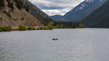 Large lake surface surrounded by tall mountains, a sole person in a kayak rowing on the water
