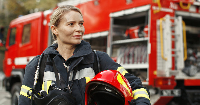 Portrait of young woman firefighter standing near fire truck.