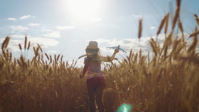 Cute girl playing with toy airplane in the wheat field at sunset. Silhouette of child playing with toy airplane on outdoor. Concept travel and freedom.