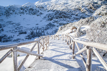 górski krajobraz, oblodzony drewniany most, śnieg i piękne niebieski niebo