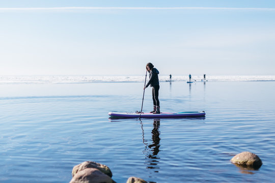 Attractive caucasian woman in black wetsuit paddle on SUP board with an oar. Female floating on stand up paddle board in the sea. In the background ice floes. Winter season and active leisure concept.