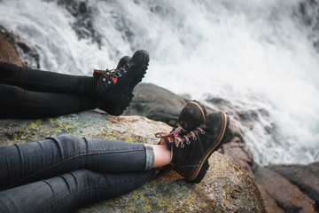 Chicas con botas sentadas en una roca al lado de un rio.