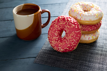 Colorful donuts and chocolate cup on dark wooden background. Morning breakfast.
