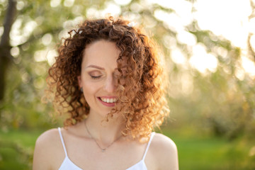 Close up portrait of young smiling attractive woman with curly hair in green flowering spring park. Pure emotions.