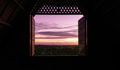 Window opens from dark room to beautiful sunrise view over jungle