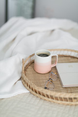 Fototapeta na wymiar Coffee in pink mug, notebook, and glasses on tray sitting on bed, coffee in bed, pink bedroom decor