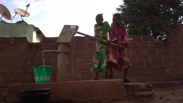 Two Joyful African Girls Pumping Water At The Community Well 