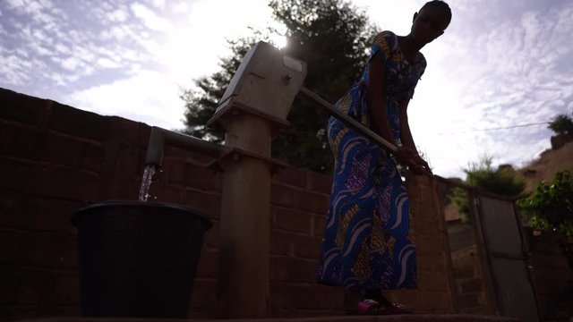 Silhouette Of An African Girl Pumping Water At The Community Well 