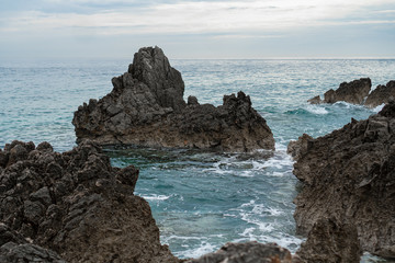 Rock sticking out of the sea in the background of gray sky and horizon