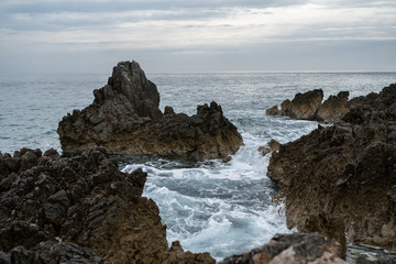 Fototapeta na wymiar Rock sticking out of the sea in the background of gray sky and horizon
