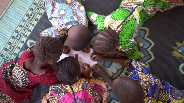 Birds Eye View On Five Small African Children Lying On The Carpet Making a Design On a Piece of Paper