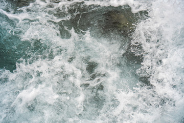 Raging blue water in a backwater with stones and white foam.