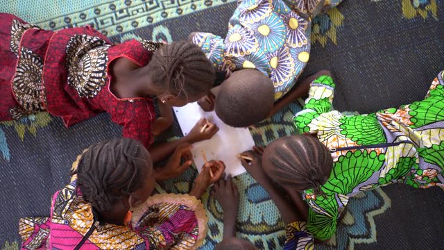 Birds Eye View On Five Small African Children Lying On The Floor Coulouring a Design