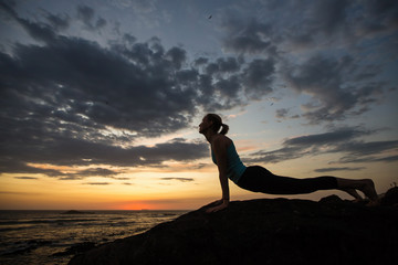 Yoga woman doing fitness exercise on the ocean coast at dusk..