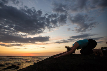 Yoga woman doing exercise on the ocean coast at dusk.