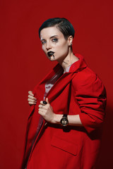 Studio photoshoot of a beautiful girl with blue hair and fashion makeup in a red jacket on a red background. Fashion style