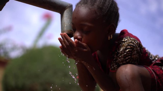 Close Up Of A Thirsty Little African Girl Drinking Water From Cupped Hands At The Village Well