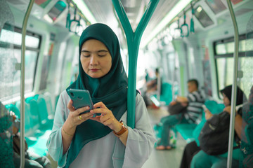 Young Muslim woman traveling inside subway train standing while using phone. Transportation and...