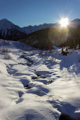 Winter hiking in Aosta Valley, Cogne, Italy. The sun is setting behind the mountains.  Backlit shot with the sun inside the frame.