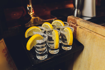 Three tequila shots with lemon and salt on wooden background.