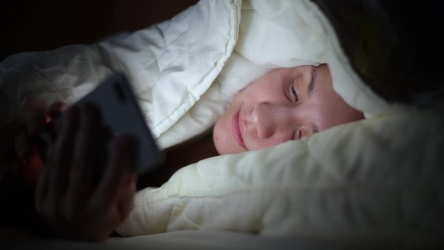 The girl lies under the covers at night and flips through the news line in the smartphone due to sleeplessness, static