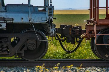 Close up of train coupler connecting two wagons of a Canadian freight or cargo train. Green fields...
