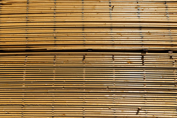 A textured background filling the frame with long and thin wooden planks. Pine boards treated and stored outside a sawmill. Ready for transport.