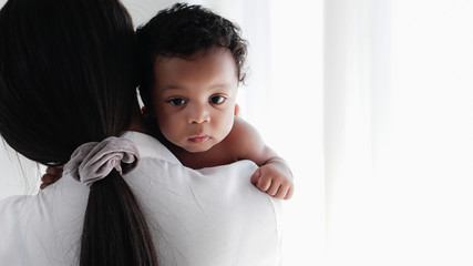 asian mother holding her black mixed race baby girl in white room