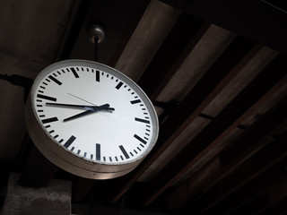 Simple old round clock hanging from wooden ceiling decoration in cafe.