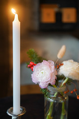 Table decorated with candle and vase of flowers and red christmas berries