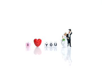Miniature / toys photography for valentines day - bride and groom  with heart shape and I love you word beads on shiny white background