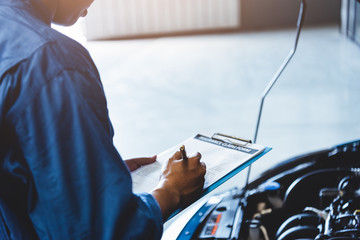 Car mechanic holding clipboard and checking to maintenance vehicle by customer claim order in auto...