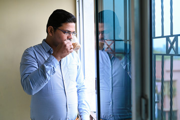 Businessman or Employee standing near window and holding a paper with a cup of Tea in other hand.