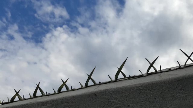 Galvanized steel metal spikes on a property border wall used for burglar proofing and security, sharp and dangerous with a beautiful background cloud time lapse.