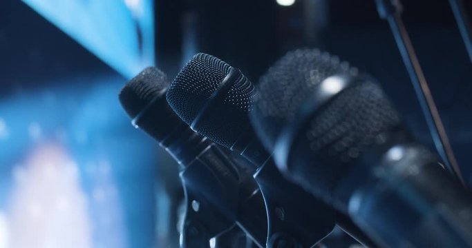 Black microphones with stand on big stage in event hall with bright backlit.
