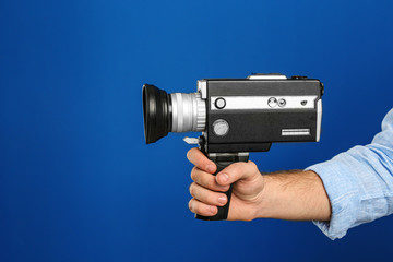 Man with vintage video camera on blue background, closeup of hand