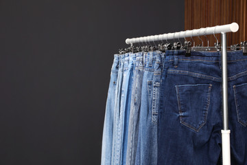 Rack with different jeans on dark grey background. Space for text