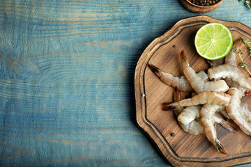 Fototapeta na wymiar Fresh raw shrimps and cut lime on blue wooden table, top view. Space for text