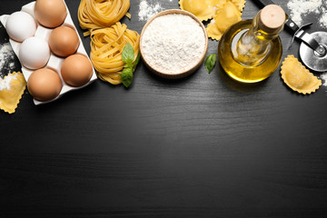 Flat lay composition with different types of pasta on black wooden table. Space for text