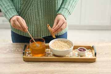 Woman adding honey to oatmeal at wooden table indoors, closeup