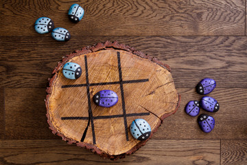 Hand made wood burn tic tac toe game with painted rock game pieces; blue and purple beetles and a wooden x and o game